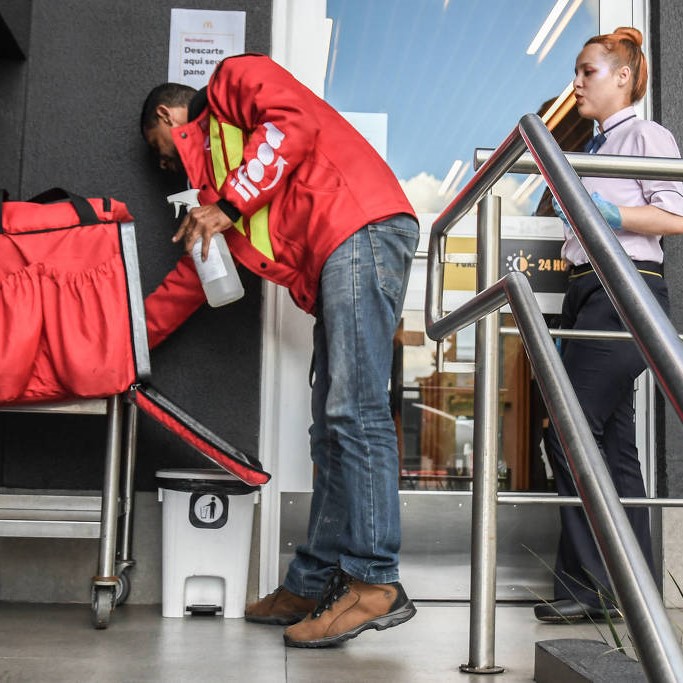 Vendas online se tornaram maioria após a pandemia; na foto, motoboy precisa limpar sua mochila de entrega antes de entrar na loja para buscar o produto